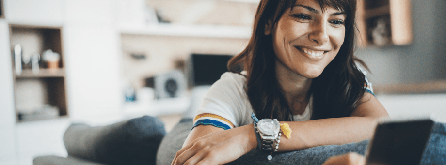 woman on couch smiling while looking at phone